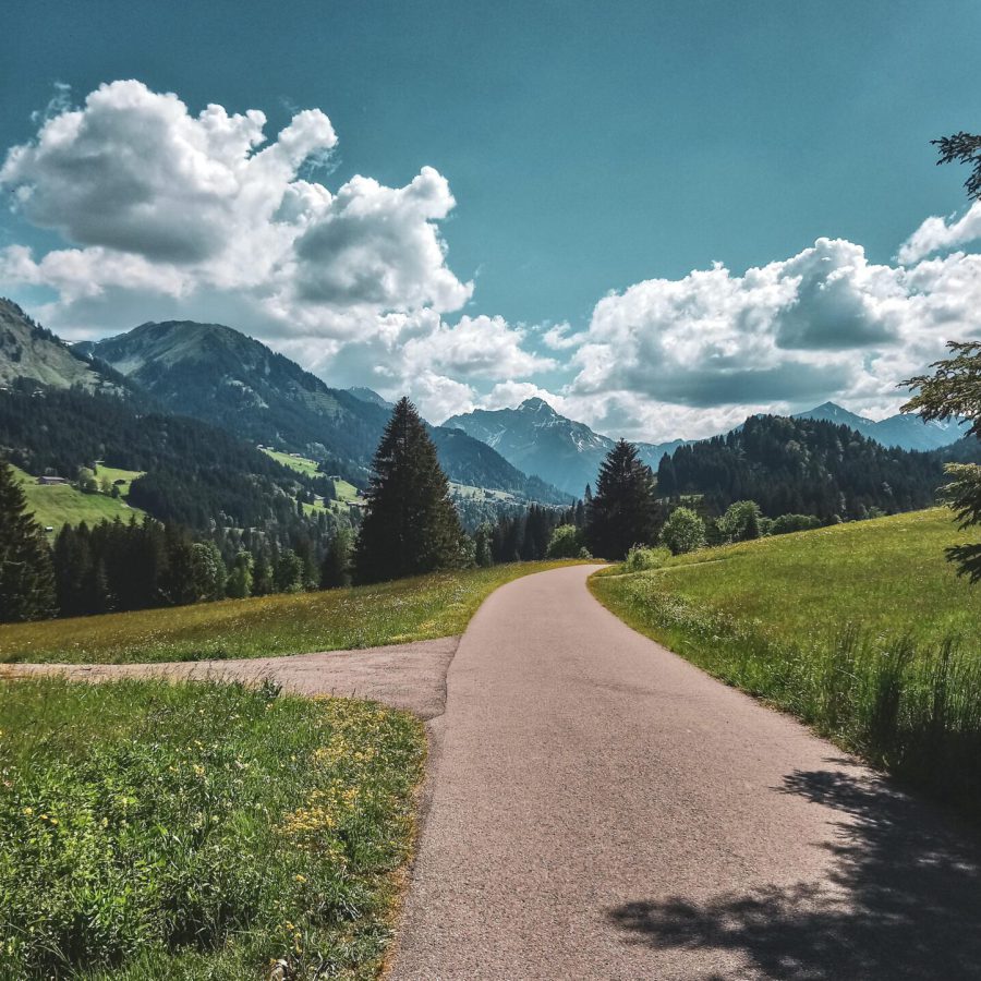 Ein heller Weg in einer schönen Naturlandschaft mit Bergen im Hintergrund und leichten Wolken am blauen Himmel