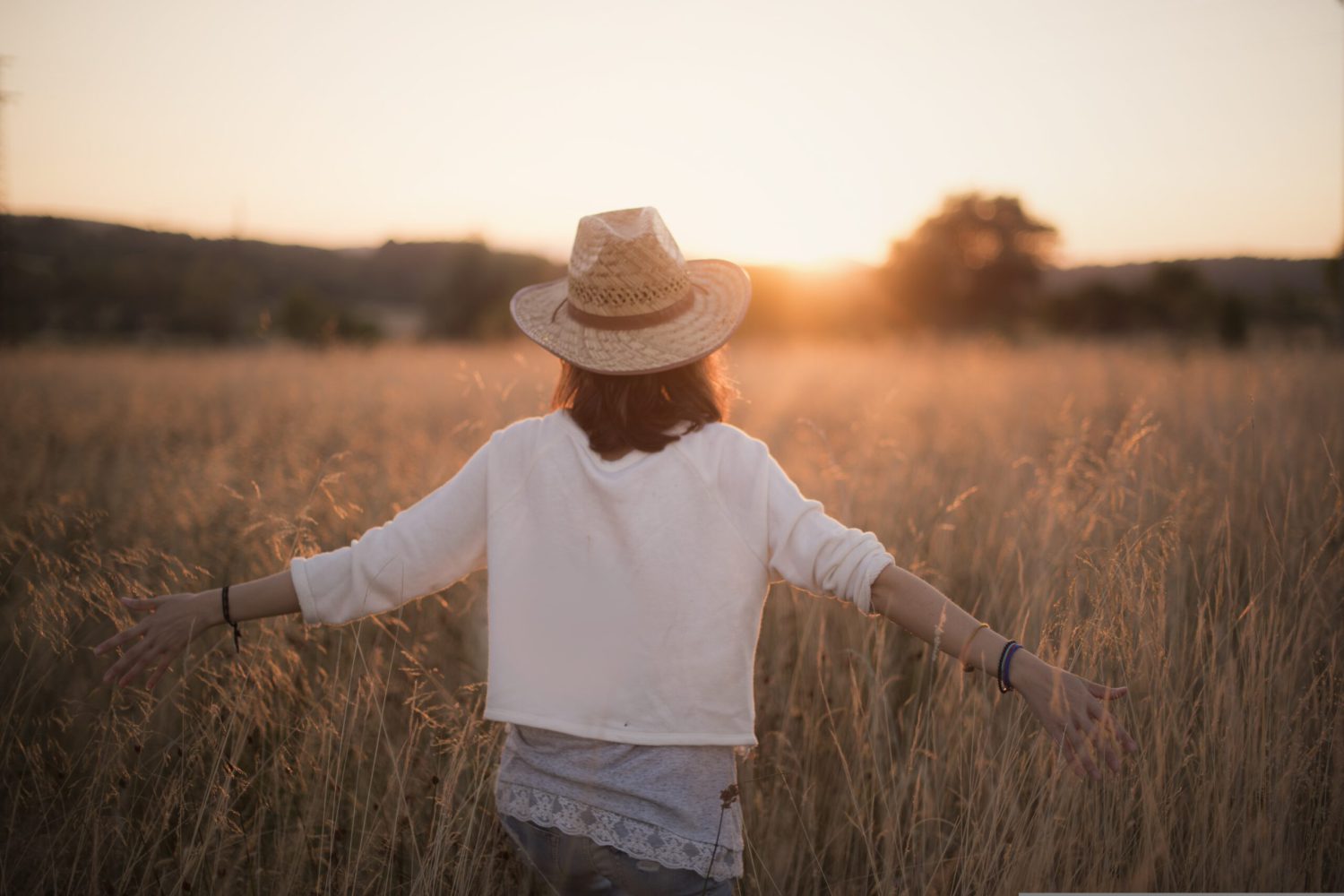 Eine Frau in der Natur mit ausgebreiteten Armen im Sonnenuntergang