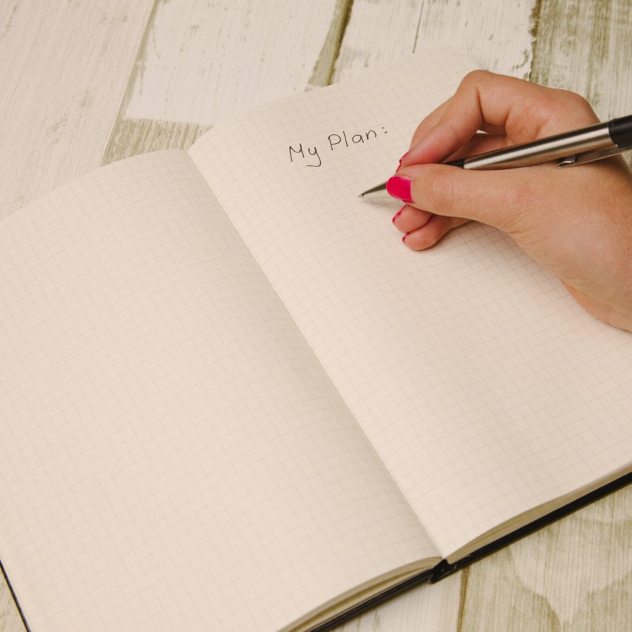 Eine Hand schreibt mit einem Stift auf Papier eine To-Do-Liste